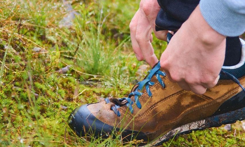 Wanderer schnürt seine Wanderschuhe auf einer Wiese