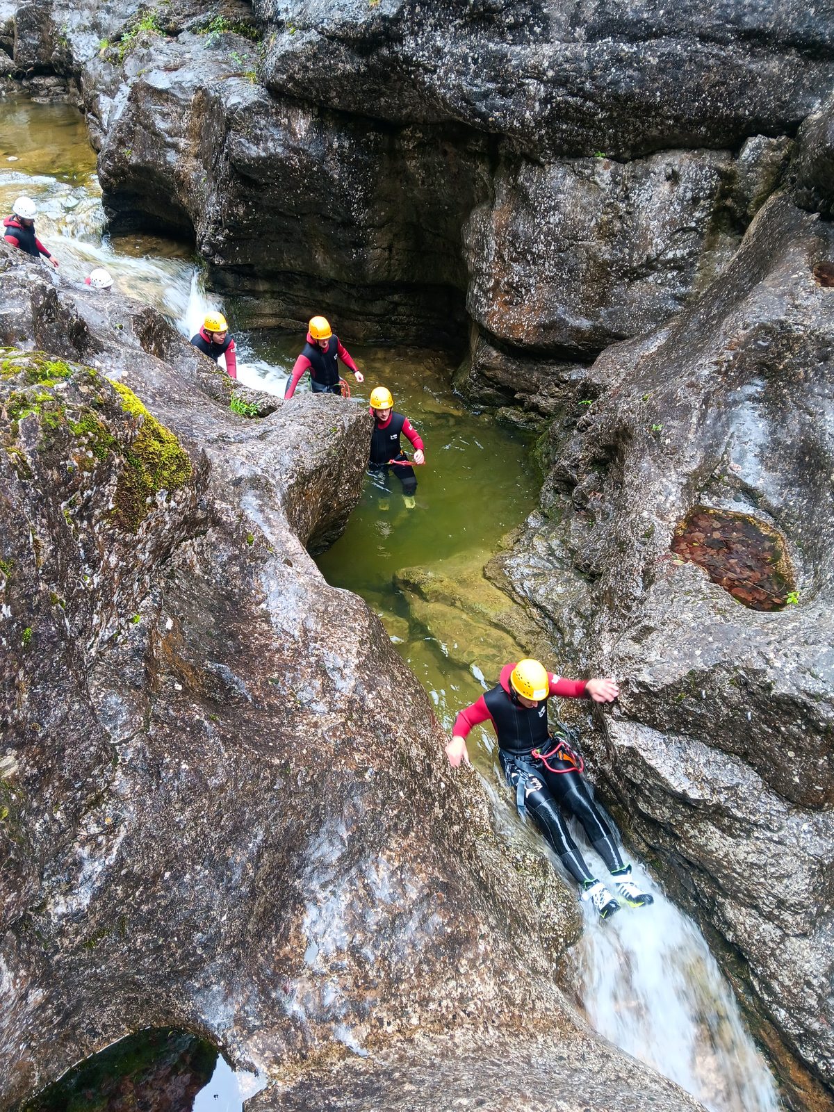 Canyoning-Teilnehmer rutscht über einen Felsen ins Wasser am Almbach